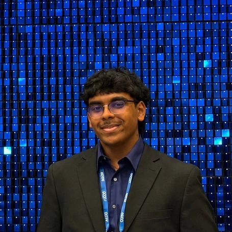 Me in a dark jacket in front of a wall of small blue square tiles, shown from the shoulders up